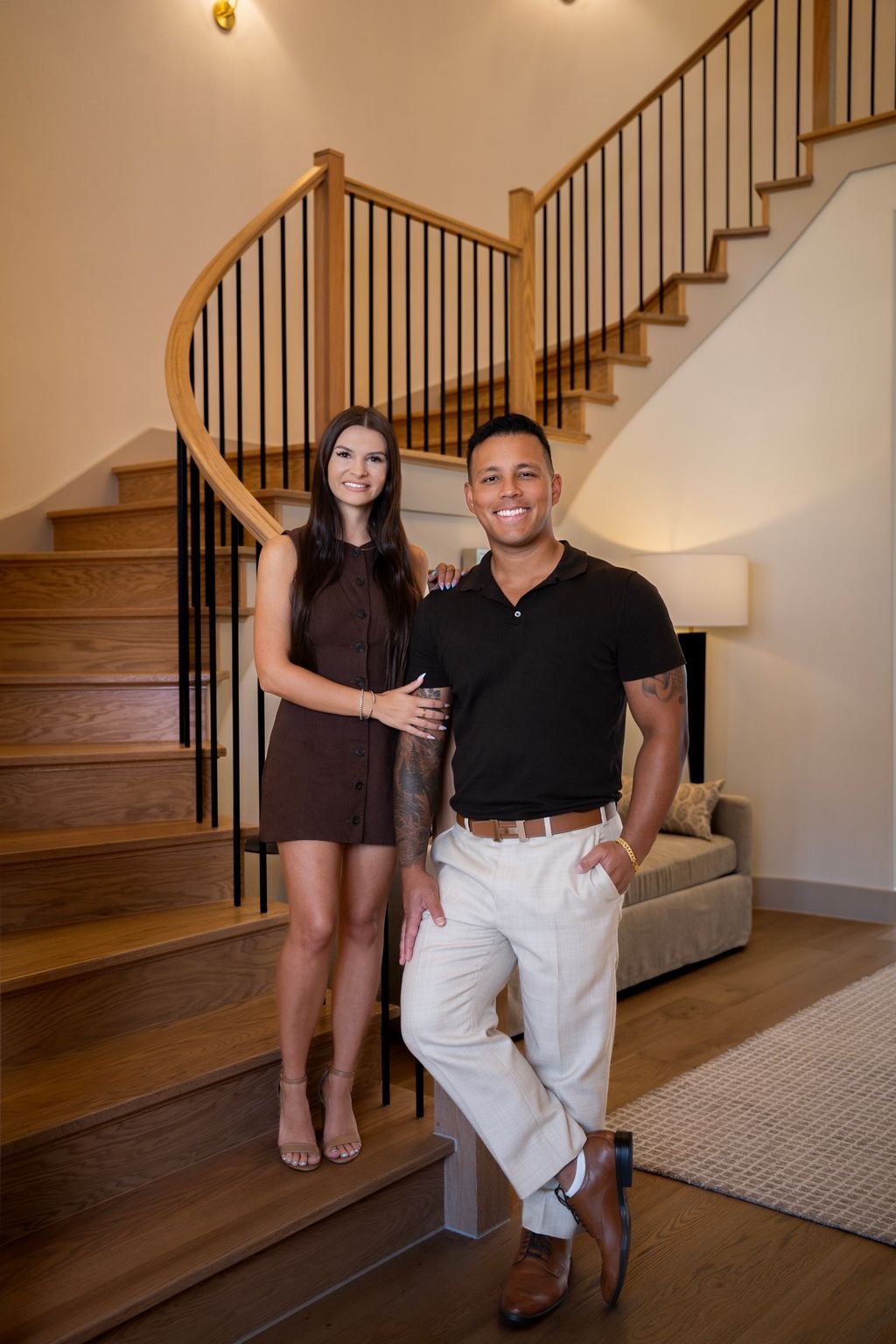 Zack and Lora standing together at the foot of a curved oak staircase